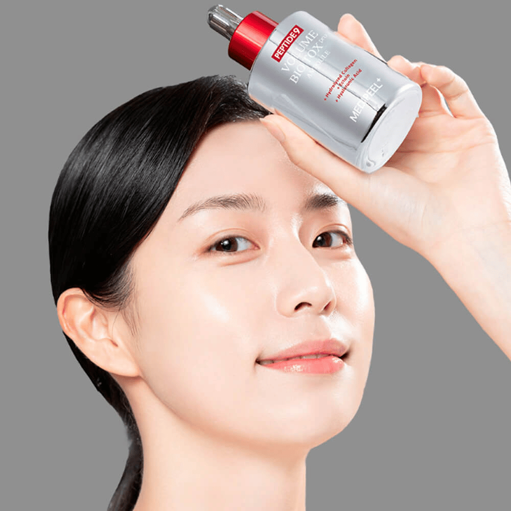 Osoba trzyma MEDI-PEEL Peptide 9 Volume Bio Tox Pro Ampoule przy czole. Skóra wygląda na nawilżoną i promienną – serum wzmacnia elastyczność i jędrność.