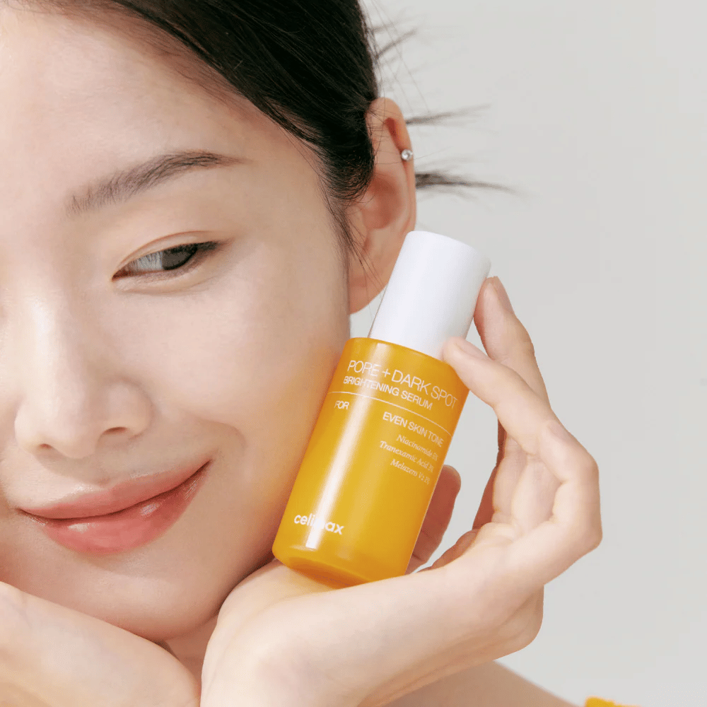 Modelka trzyma Celimax Pore + Dark Spot Brightening Serum blisko twarzy, pokazuje promienną cerę.
