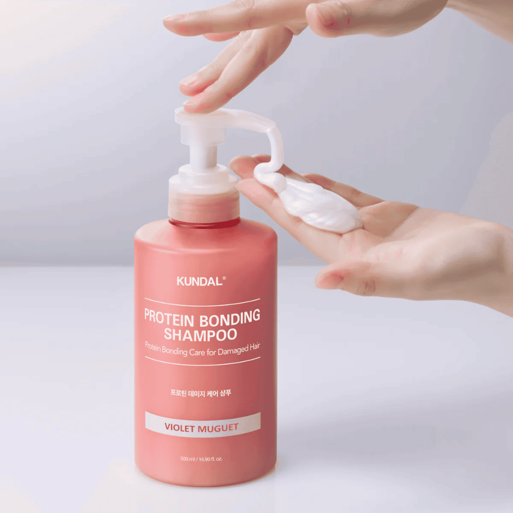 Ręka pompuje KUNDAL Protein Bonding Shampoo Violet Muguet o kremowej konsystencji, szampon regenerujący do zniszczonych włosów.