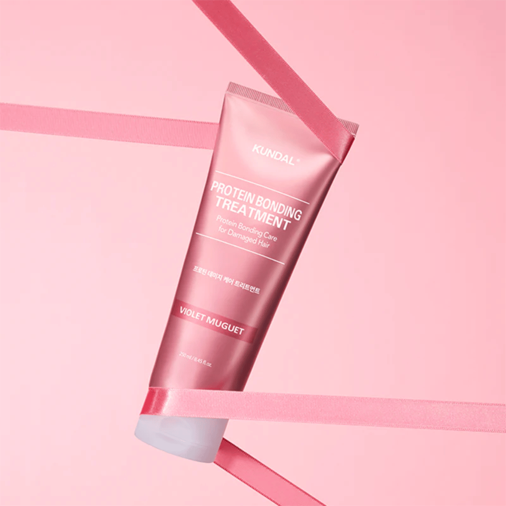 KUNDAL Protein Bonding Treatment Violet Muguet w różowej tubce 250 ml na różowym tle z dekoracyjnymi wstążkami.