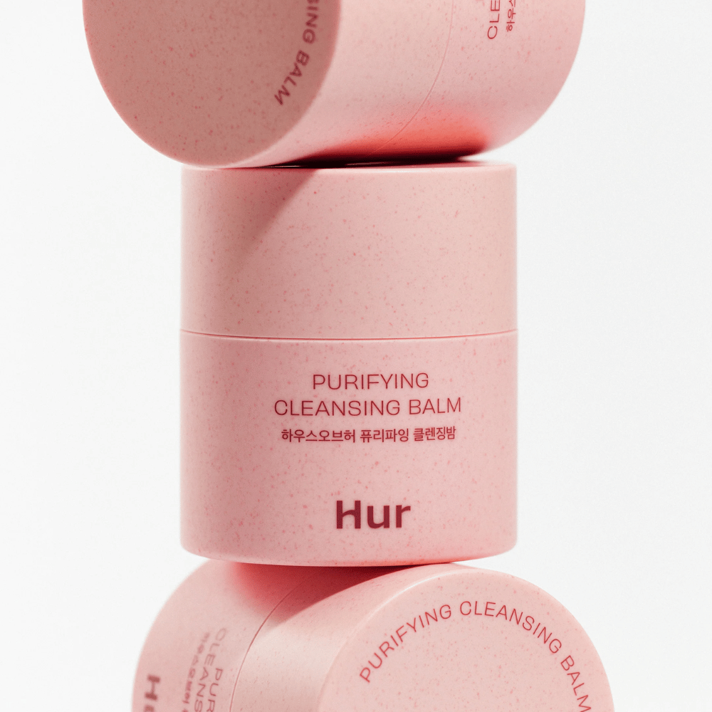 Jak Purifying Cleansing Balm w różowym opakowaniu ułożonym w studio. Oczyszczający balsam, który skutecznie rozpuszcza makijaż, sebum i zanieczyszczenia, nie wysuszając skóry.