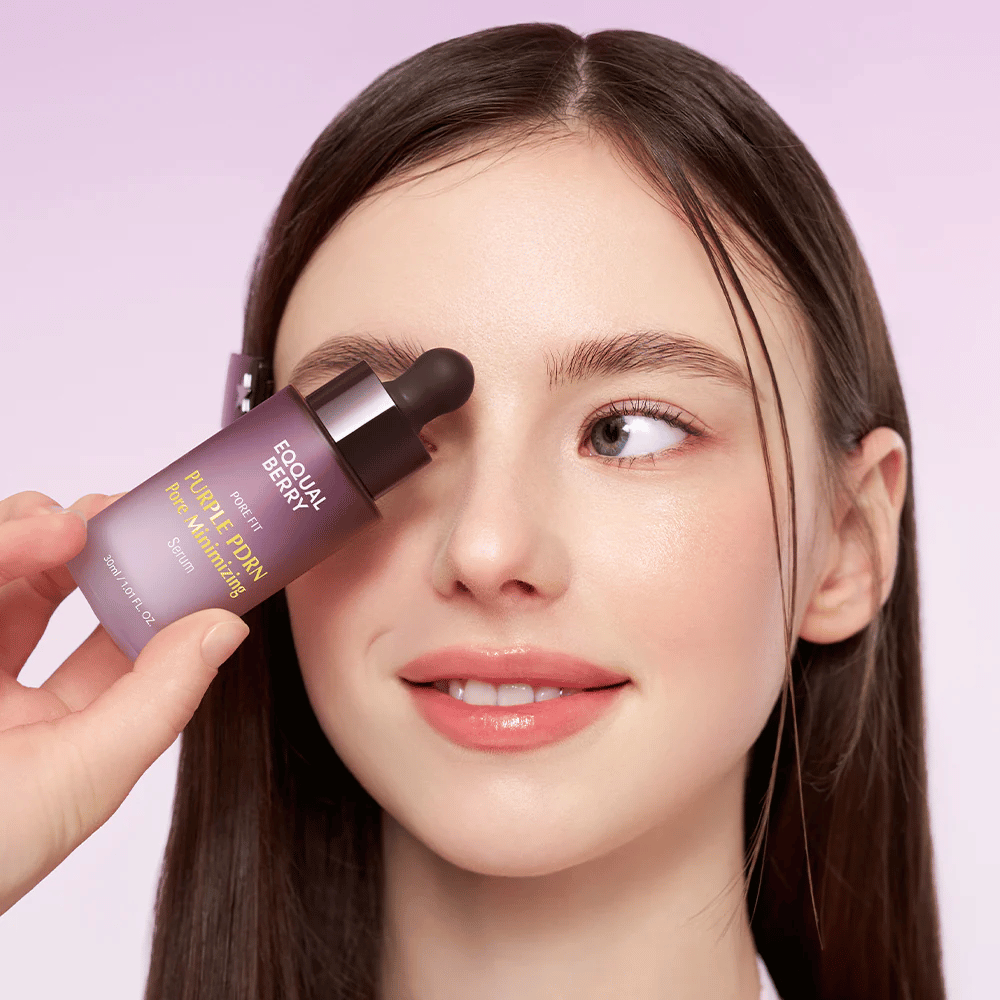 Ung kvinna med slät hy håller i en flaska Equal Berry Purple PDRN Pore Minimizing Serum mot pannan, mot en ljuslila bakgrund.