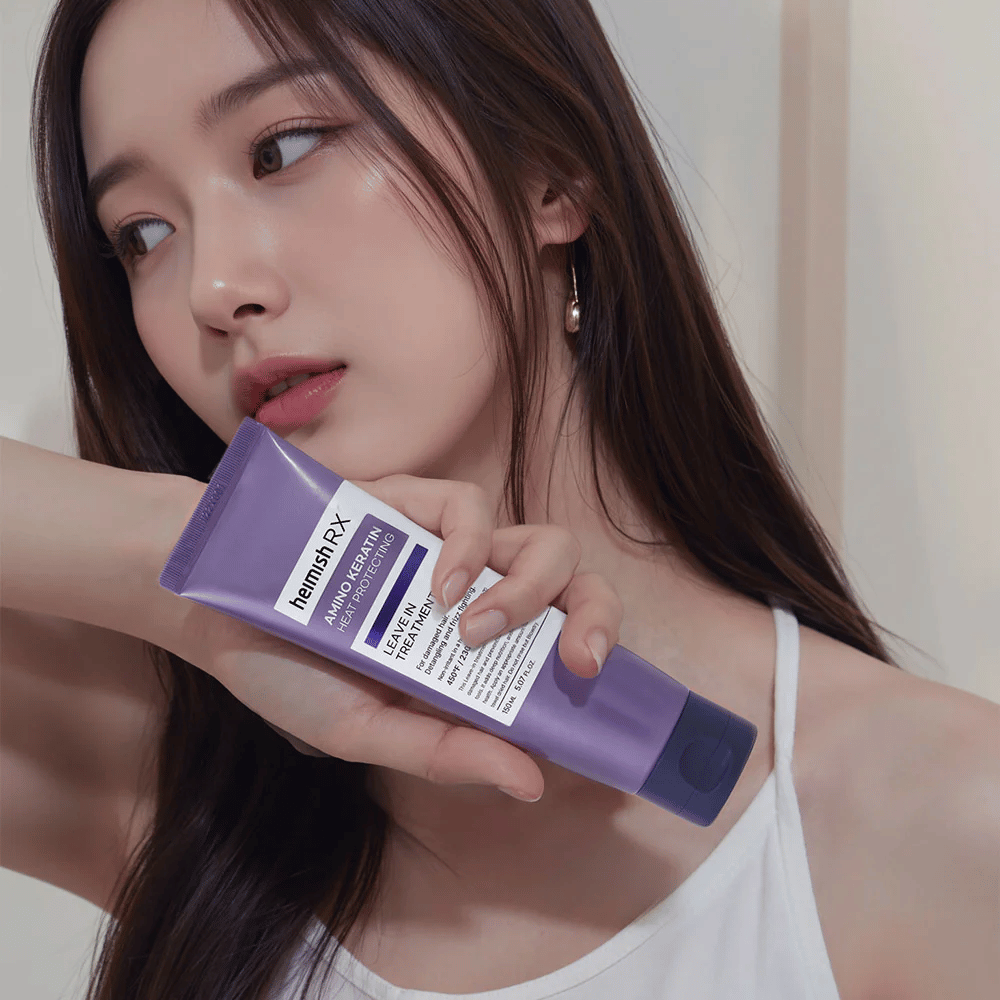 Kobieta z długimi, lśniącymi włosami trzyma Heimish RX Amino Keratin Leave-In Treatment – pokazuje produkt jako pielęgnacyjny i chroniący przed ciepłem krok w rutynie pielęgnacji włosów.
