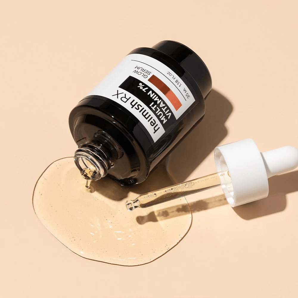 Heimish RX Multi Vitamin 7% Glow Serum leżący na beżowym tle z rozlanym wokół butelki serum i pipetą wypełnioną produktem, co podkreśla jego bogatą w składniki odżywcze formułę.