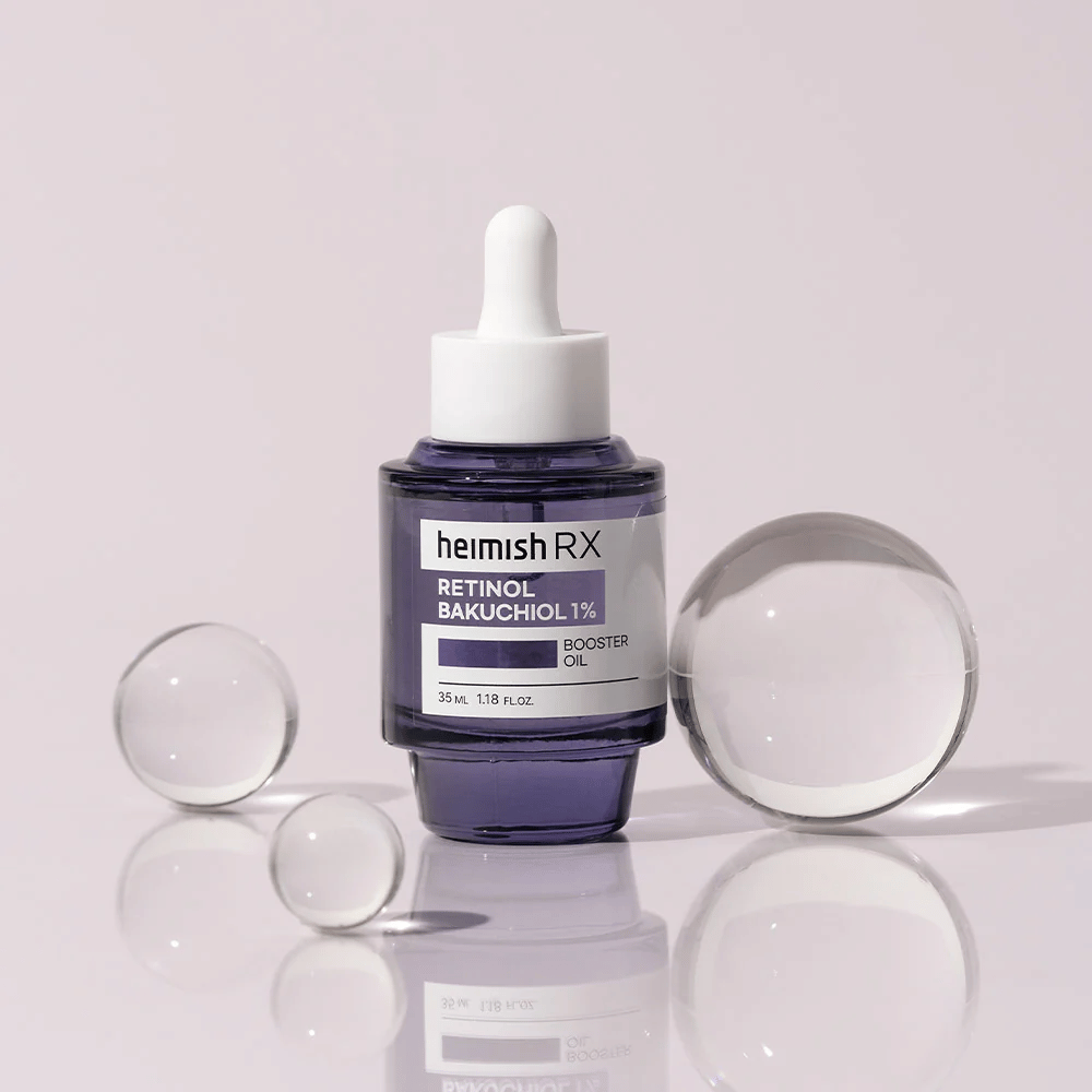 Heimish RX Retinol Bakuchiol Booster Oil 1% w eleganckiej fioletowej szklanej butelce z pipetą. Olejek jest umieszczony na refleksyjnej powierzchni z szklanymi kulkami wokół, co nadaje luksusowy i nowoczesny wygląd.