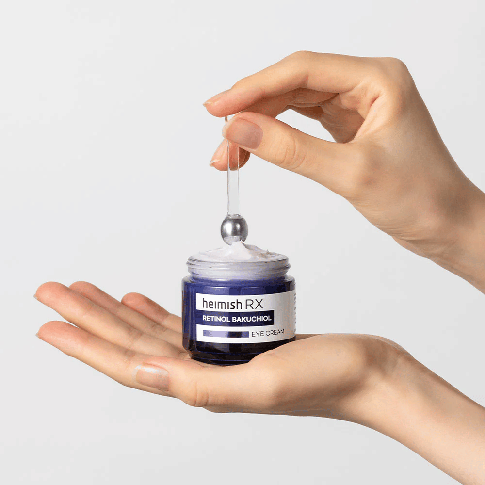 Heimish RX Retinol Bakuchiol Eye Cream w eleganckim niebieskim słoiku, podniesiony za pomocą metalowego aplikatora. Krem pod oczy z retinolem i bakuchiolem, aby zredukować drobne linie i zapewnić jędrniejszą skórę.