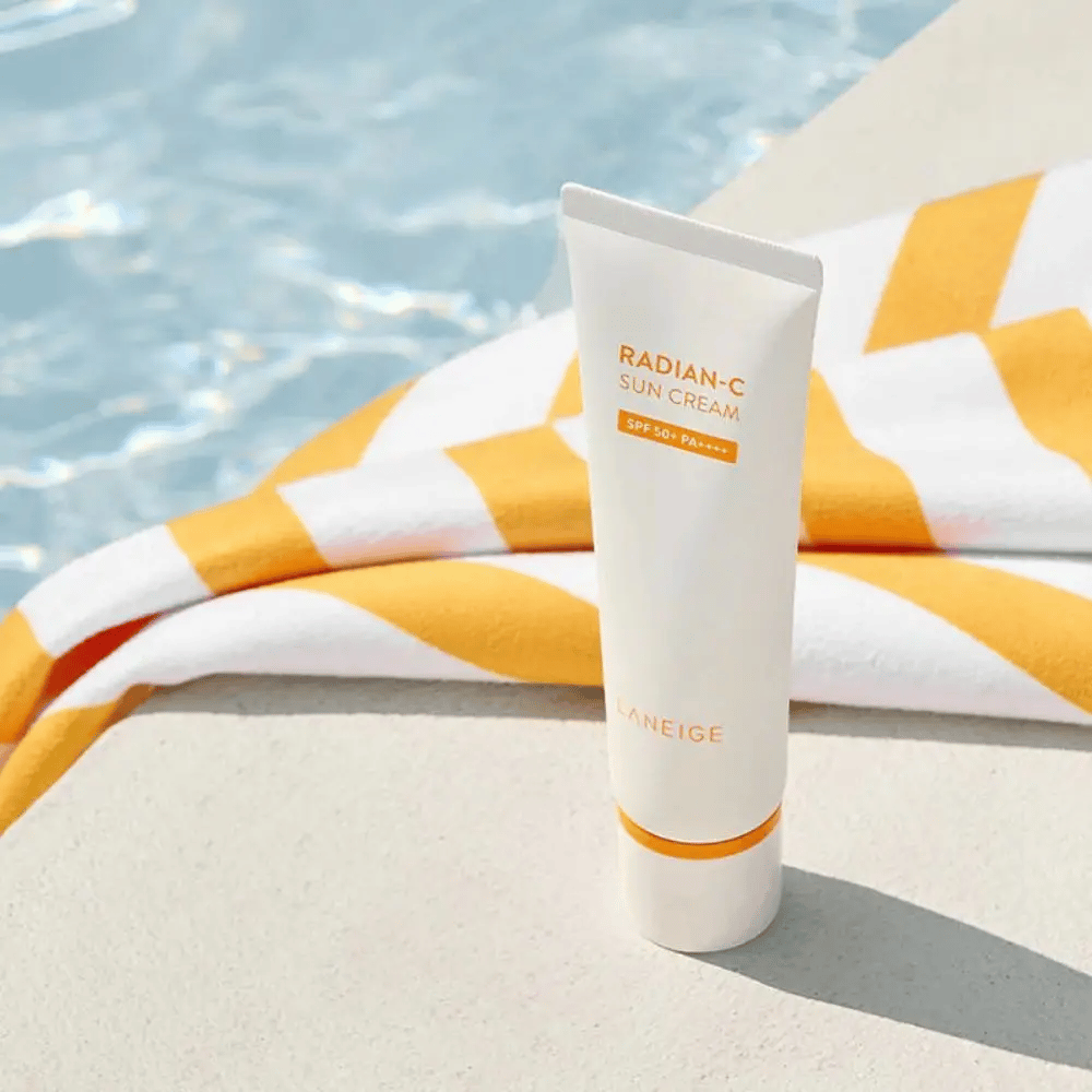 LANEIGE Radian-C Sun Cream stoi przy brzegu basenu z żółto-białym ręcznikiem w tle.