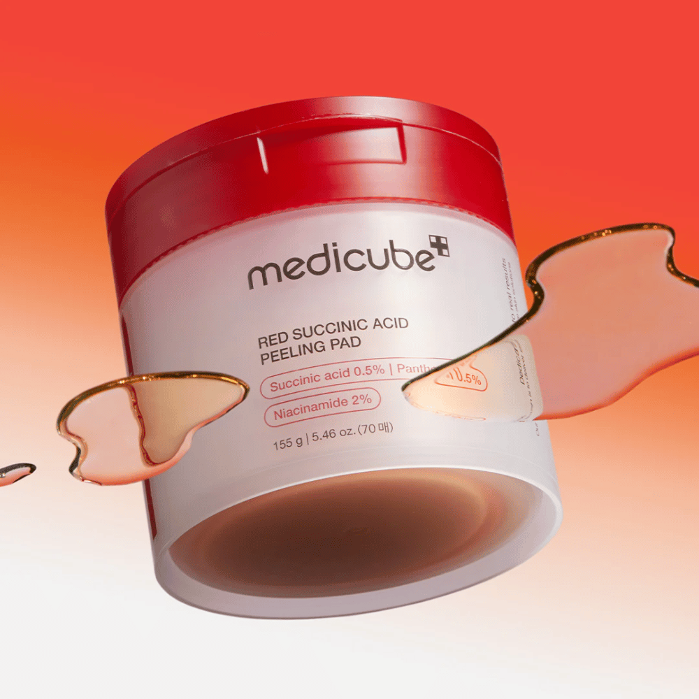 Medicube Red Succinic Acid Peeling Pad w białym i czerwonym słoiku, umieszczony na tle gradientowym w kolorze czerwonym i pomarańczowym. Produkt zawiera kwas bursztynowy i niacynamid do złuszczania i poprawy skóry. Płynna tekstura widoczna wokół słoika.