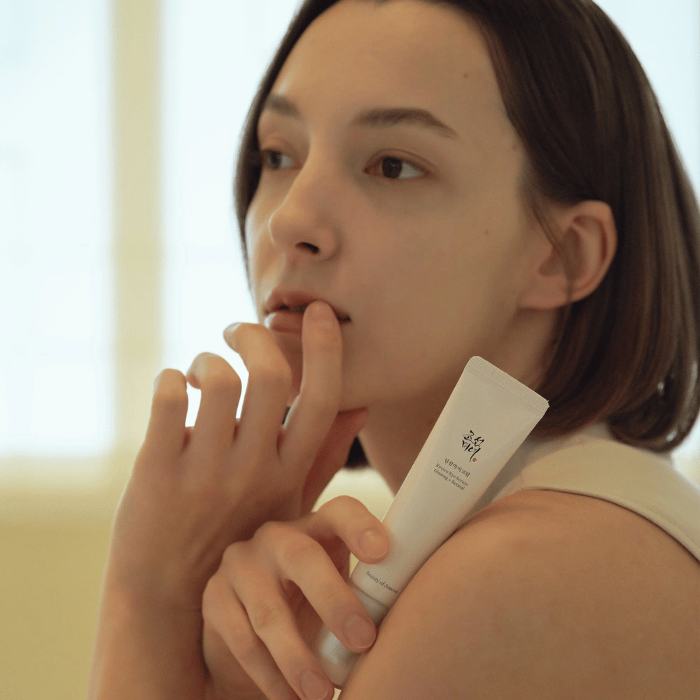 Modelka trzyma Beauty of Joseon Revive Eye Serum i delikatnie aplikuje na skórę dla nawilżonego i gładkiego konturu oczu.