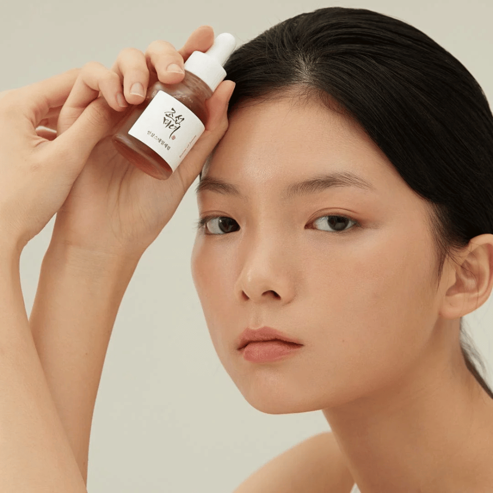 Modelka trzyma Beauty of Joseon Revive Serum przy policzku – odżywcze serum z żeń-szeniem i krem ze śluzem ślimaka.