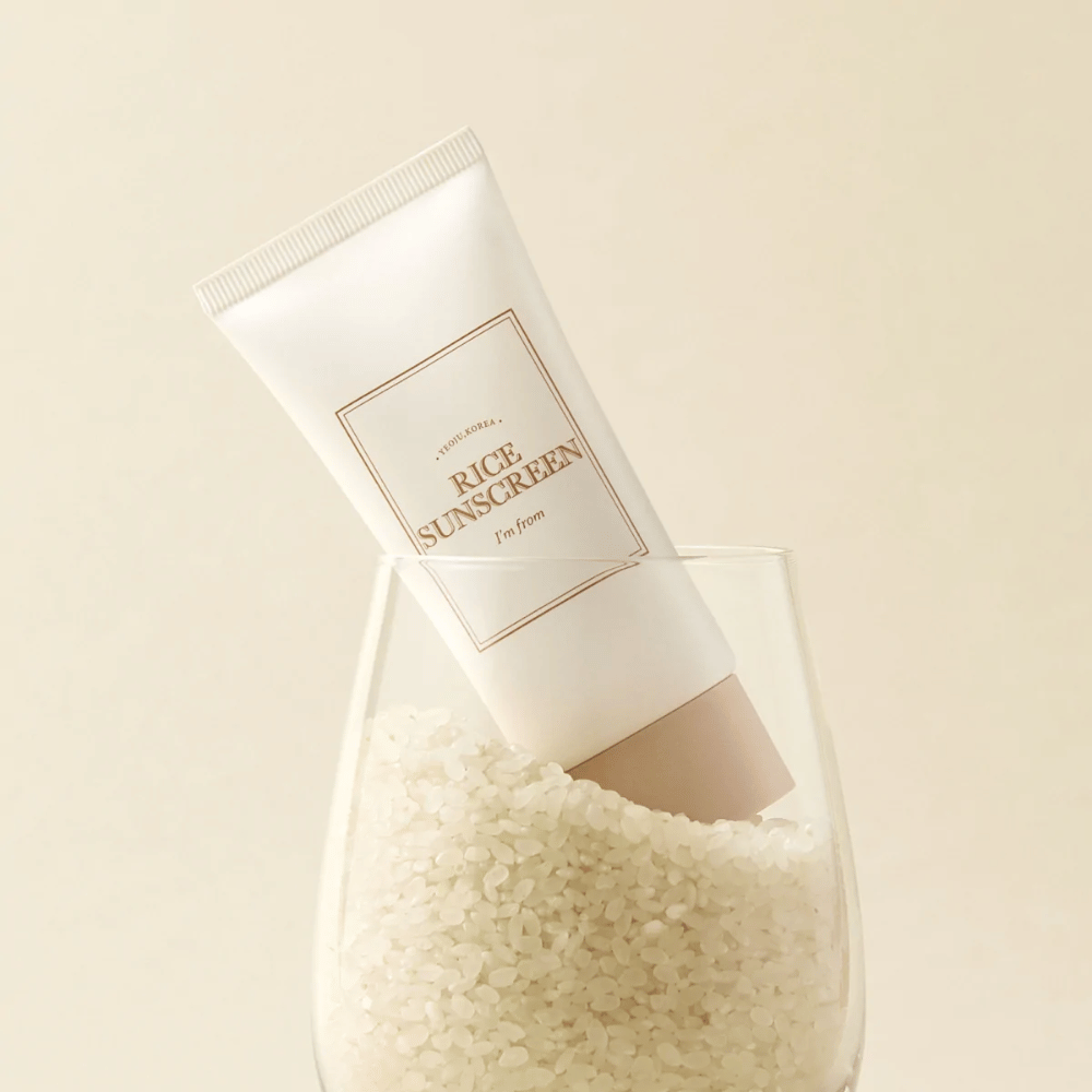 Tuba z "I'm from" Rice Sunscreen, SPF50+ PA++++, umieszczona w szklance z ziarnami ryżu.