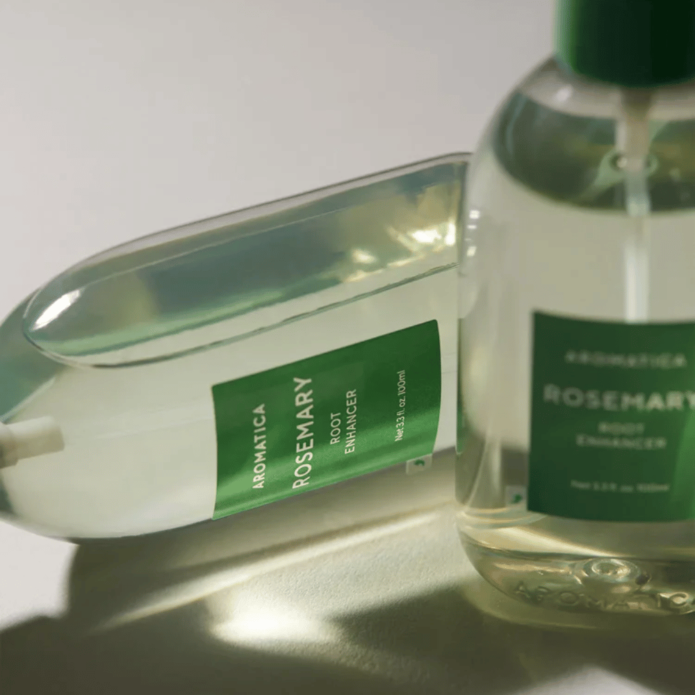 Dwie butelki AROMATICA Rosemary Root Enhancer z przezroczystą nasadką ochronną i zieloną etykietą. Zbliżenie podkreśla premium design produktu i koncepcję naturalnej pielęgnacji włosów.