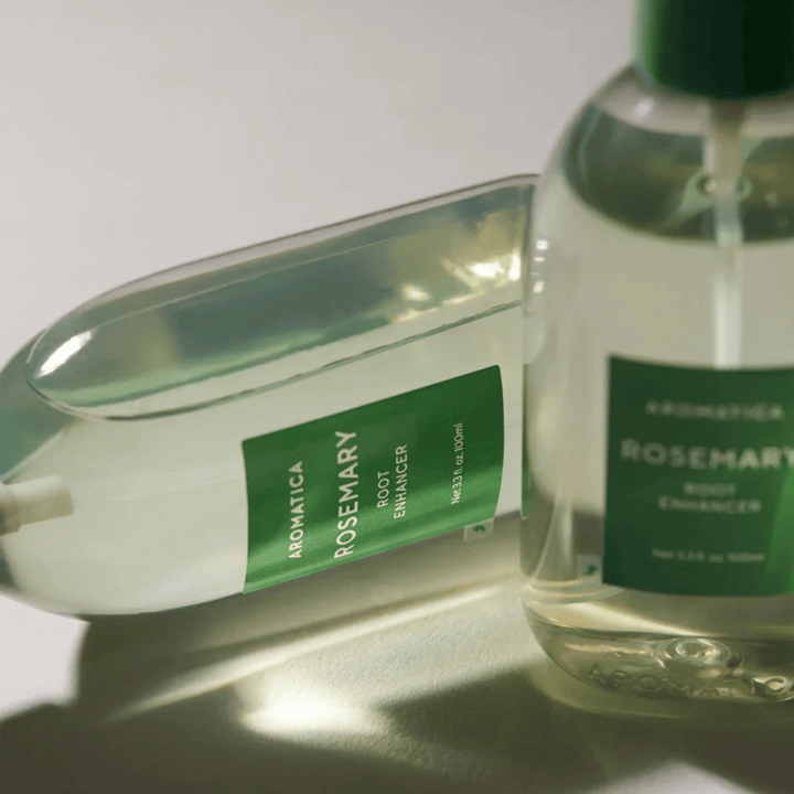 Dwie butelki AROMATICA Rosemary Root Enhancer z przezroczystą nasadką ochronną i zieloną etykietą. Zbliżenie podkreśla premium design produktu i koncepcję naturalnej pielęgnacji włosów.