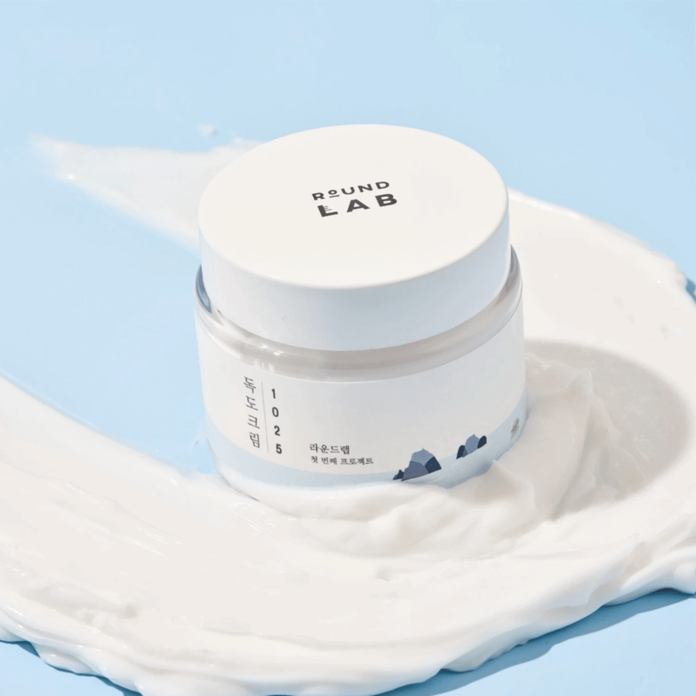 Słoik z Round Labs 1025 Dokdo Cream 80 ml, który zapewnia nawilżenie, umieszczony na żywym niebieskim tle.