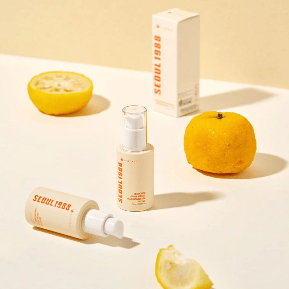 Kilka butelek i opakowań Seoul 1988 Glow Serum ułożonych z całymi i połówkami owoców yuja w tle.