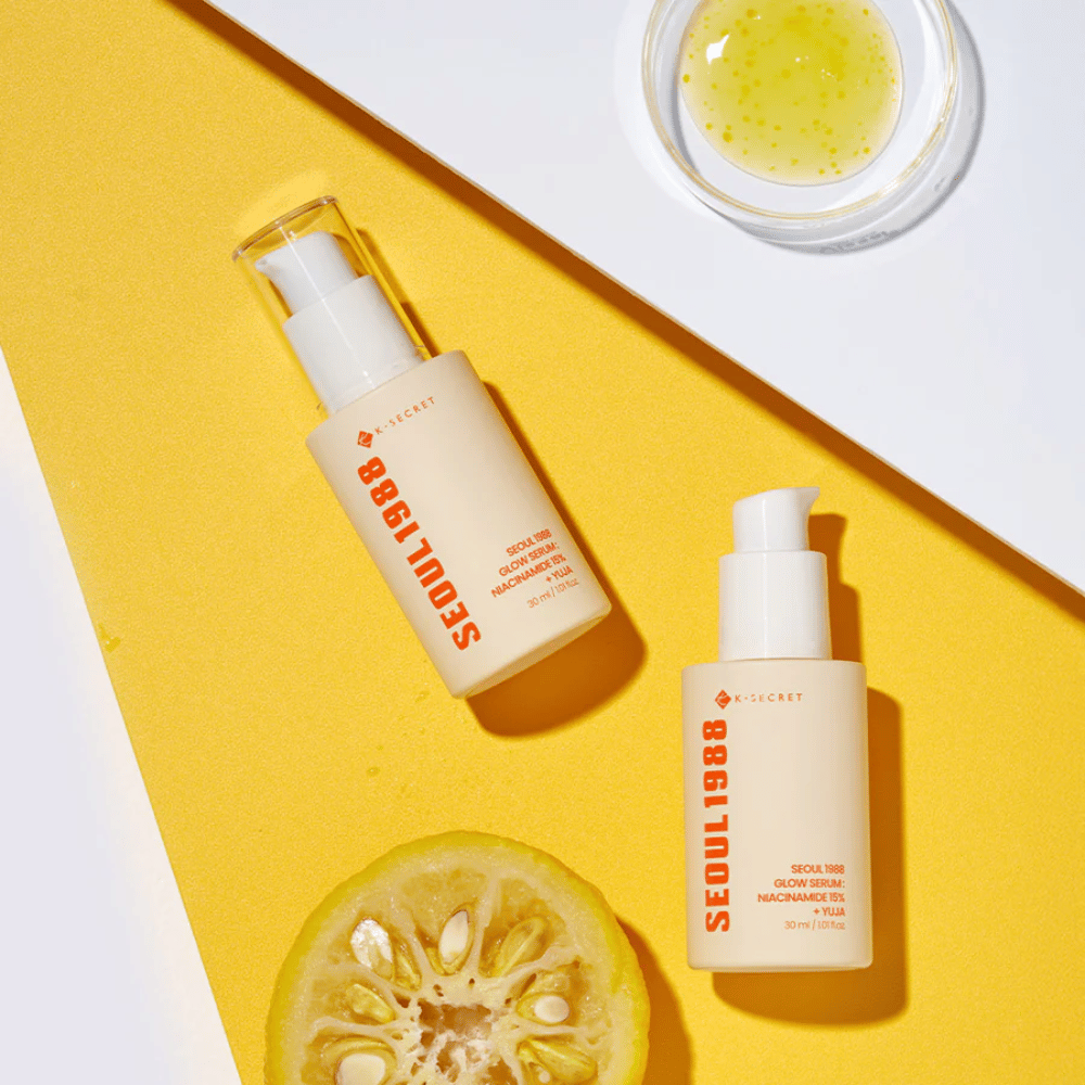 Dwie butelki Seoul 1988 Glow Serum umieszczone na żółtym tle wraz z miseczką z żółtym serum i połówką owocu cytrusowego.