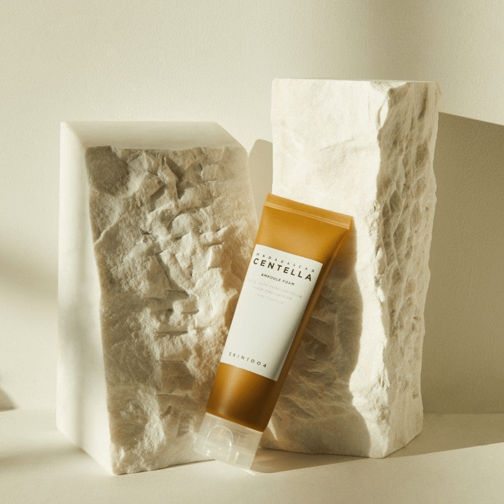 SKIN1004 Madagascar Centella Ampoule Foam stojący na jasnych kamiennych blokach w naturalnym świetle słonecznym, z brązowo-białym projektem tuby i eleganckim minimalizmem.