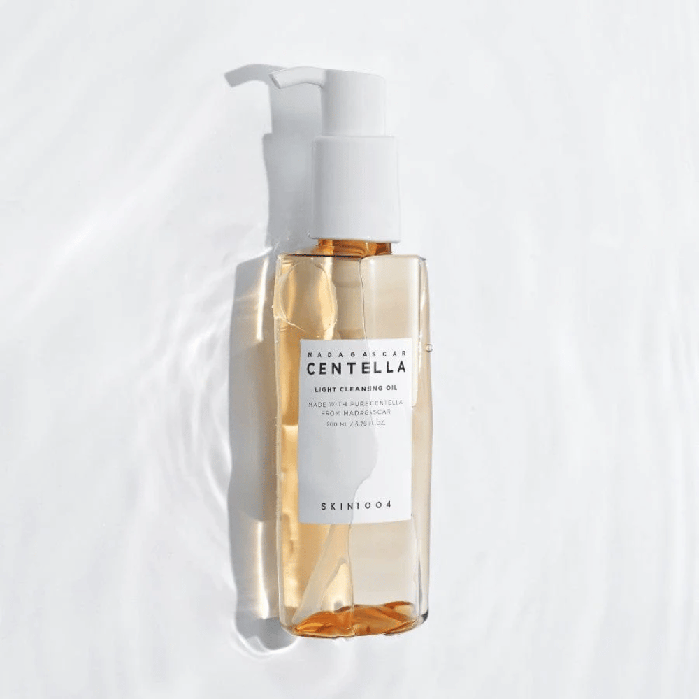 SKIN1004 Madagascar Centella Light Cleansing Oil na białym tle z delikatnymi refleksami wodnymi, które podkreślają przezroczystą butelkę i złocistą zawartość.