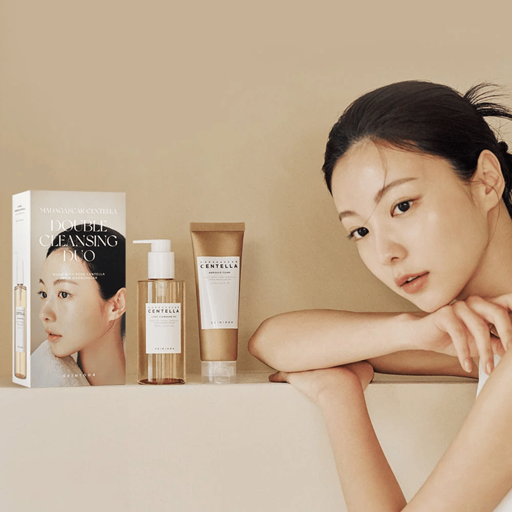 SKIN1004 Madagascar Centella Double Cleansing Duo Set z kartonem, olejowym środkiem czyszczącym, pianką oczyszczającą i modelem z nawilżoną skórą na beżowym tle.