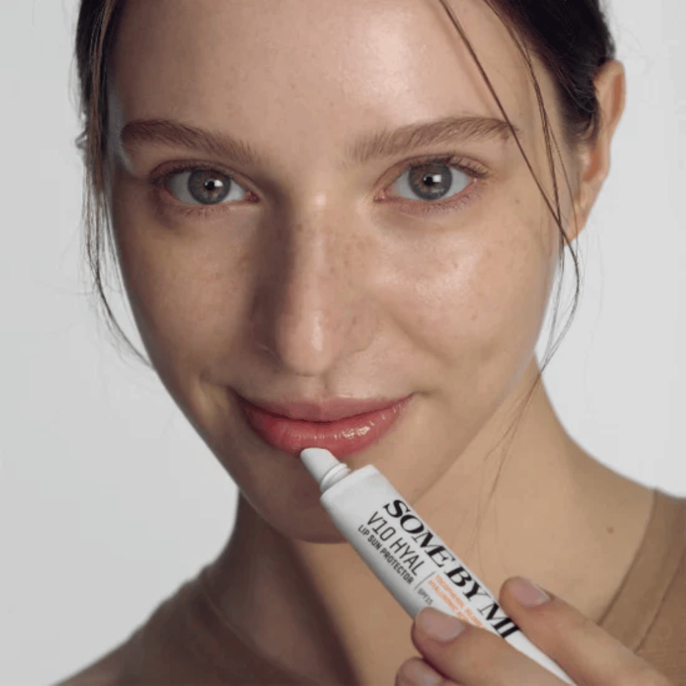 Kobieta trzyma tubkę V10 Hyal Lip Sun Protector SPF15 7ml balsamu do ust z filtrem przeciwsłonecznym i nawilżającym, od SOME BY MI.