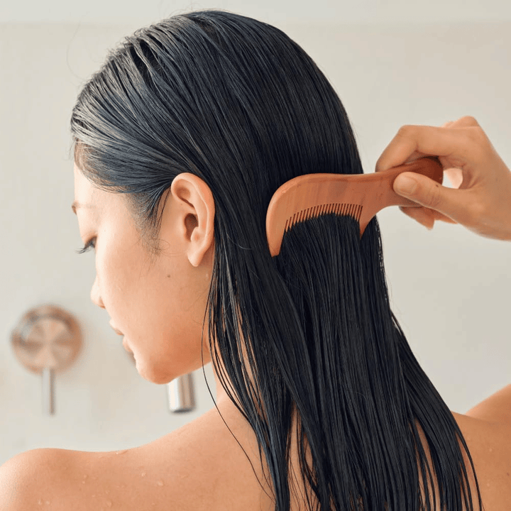 Osoba przeczesuje długie, mokre włosy szerokim grzebieniem po nałożeniu Heveblue Salmon Pullkeratin Centella Hair Treatment. Ilustruje działanie rozplątujące i zmiękczające, zapewniające gładszy efekt.