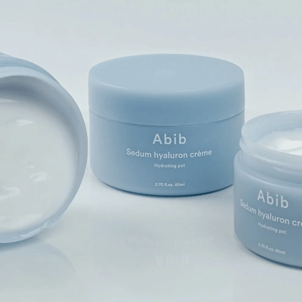 Trzy słoiki Abib Sedum Hyaluron Crème Hydrating Pot 80 ml w jasnoniebieskim minimalistycznym designie, z których jeden otwarty słoik pokazuje kremową białą konsystencję.