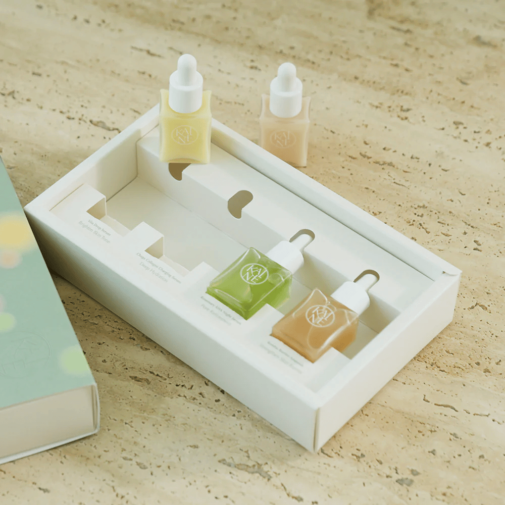 Cztery kolorowe butelki z serum od KAINE Serum Discovery Kit z pipetą, zaprojektowane, aby sprostać różnym potrzebom skóry w minimalistycznym i eleganckim opakowaniu.
