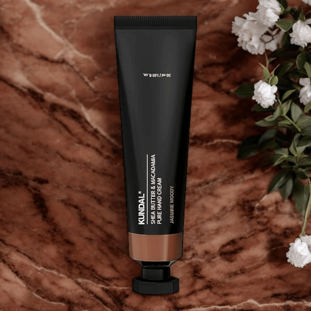 KUNDAL Shea Butter & Macadamia Pure Hand Cream Jasmine Woody umieszczony na marmurze z kwiatami – odżywczy krem do rąk, który pielęgnuje suche dłonie i zapewnia elegancki zapach jasmine woody.