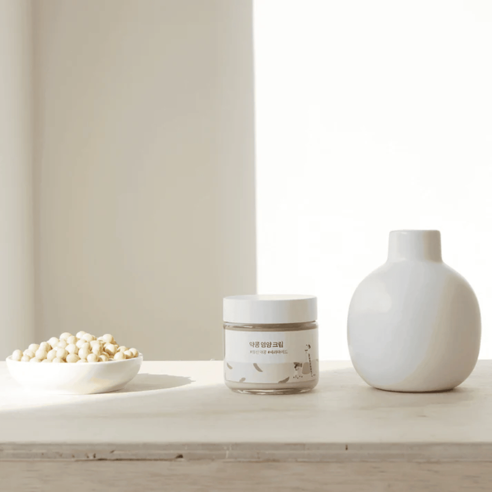Mixsoon Soybean Nourishing Cream stoi na drewnianym stole obok wazonu i soi. Minimalistyczny, nawilżający krem z naturalnymi składnikami.