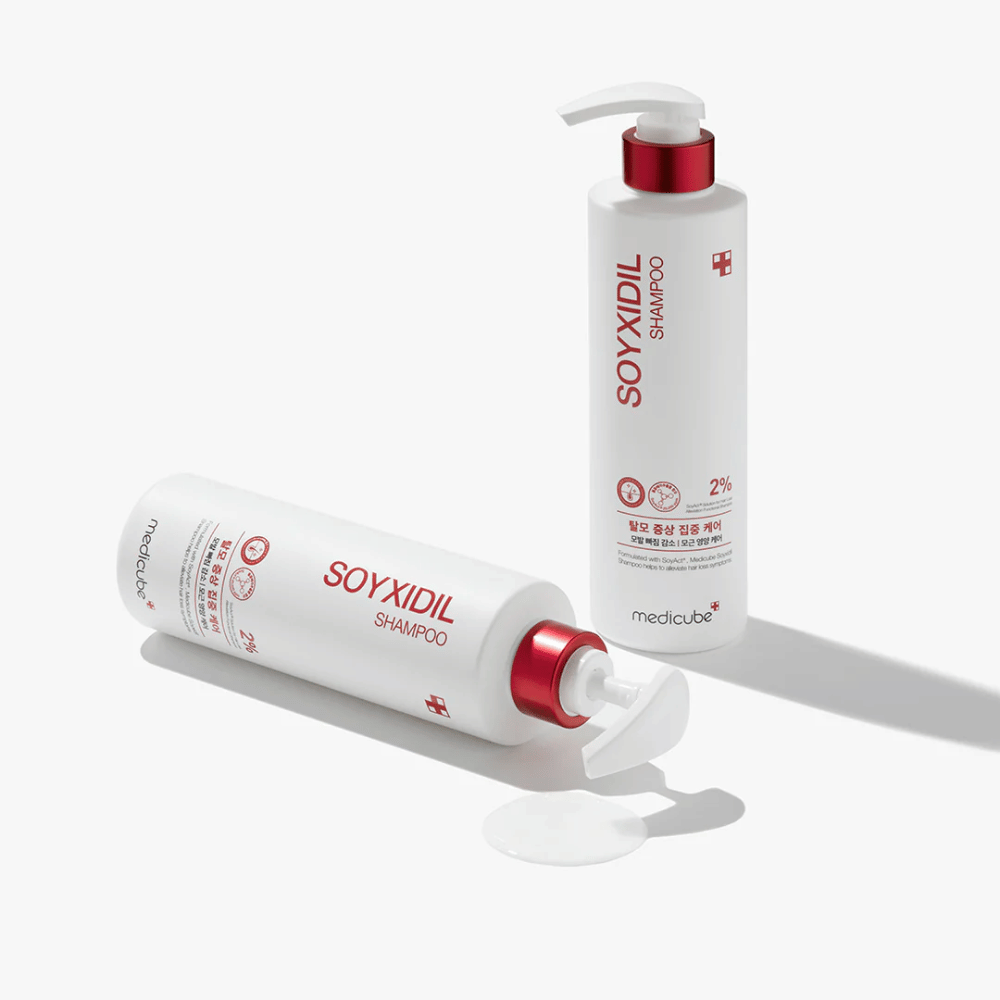 Dwie butelki Medicube Soyxidil Shampoo w białym i czerwonym wzorze, jedna stojąca, druga leżąca z rozlanym szamponem obok.