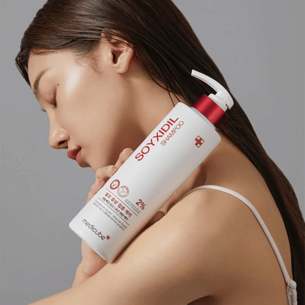 Kobieta z długimi włosami opiera głowę o butelkę Medicube Soyxidil Shampoo, która wzmacnia skórę głowy i przeciwdziała wypadaniu włosów.