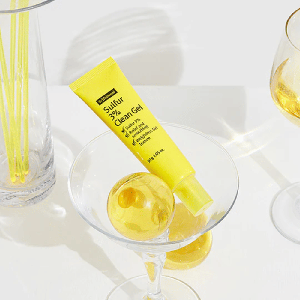 By Wishtrend Sulfur 3% Clean Gel w żółtej tubce umieszczonej w szklance koktajlowej z żółtą sferą, otoczoną eleganckimi szklankami na białym tle.