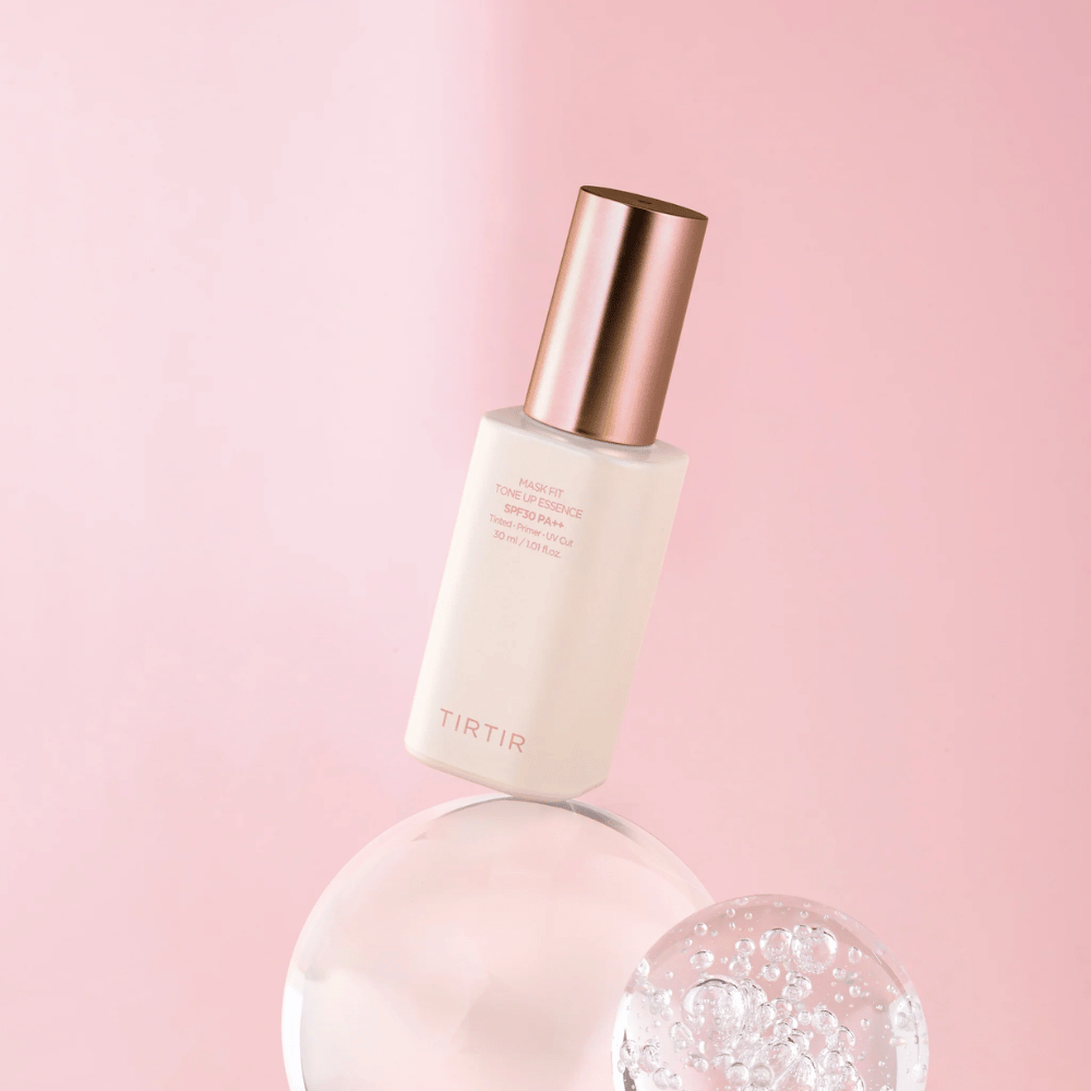 Zdjęcie przedstawia butelkę "TIRTIR MASK FIT TONE UP ESSENCE" z SPF30 PA++ na różowym tle, co daje poczucie miękkości i kobiecości.