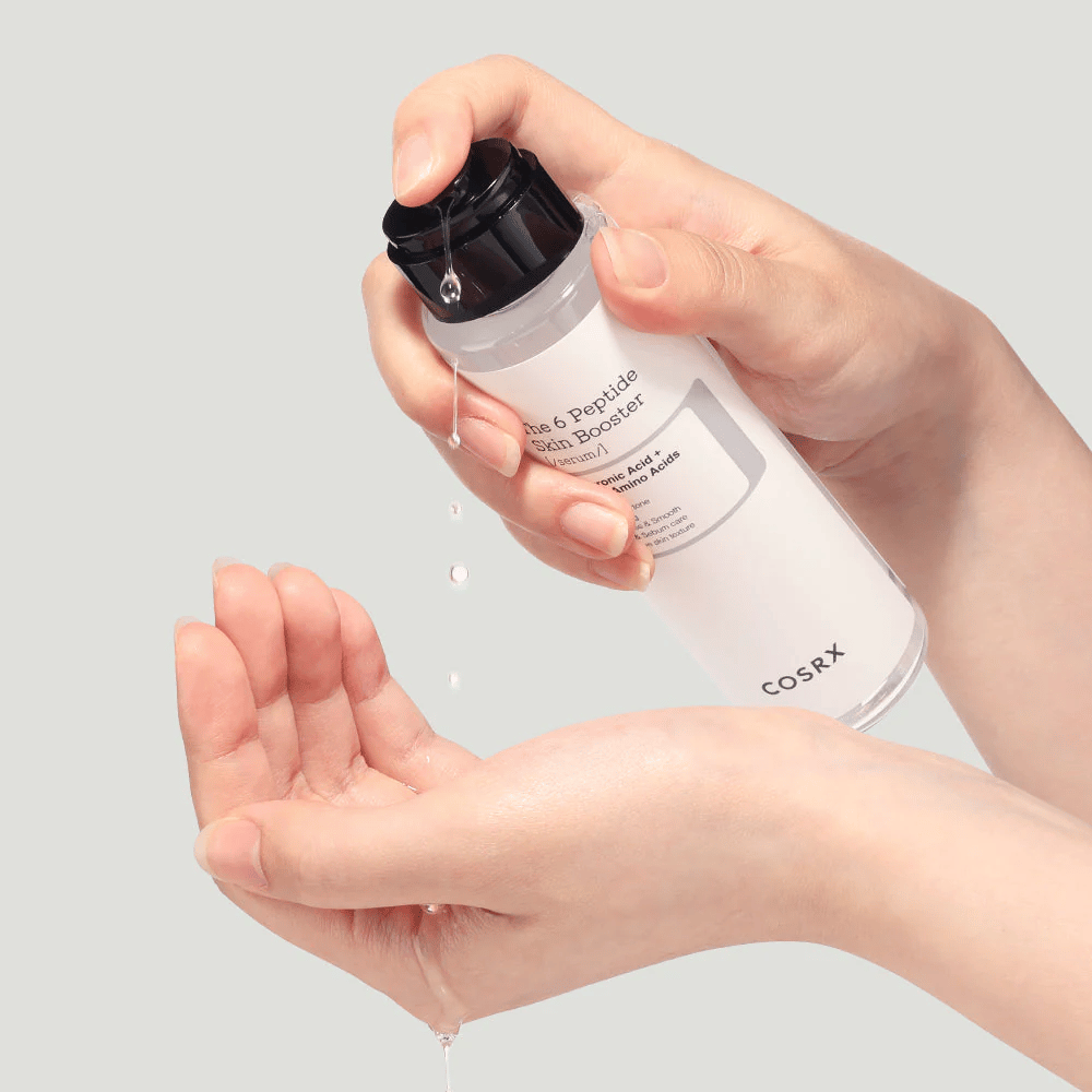 Ręce wylewające produkt do pielęgnacji skóry z przezroczystej butelki z napisem "The Peptide Skin Booster".