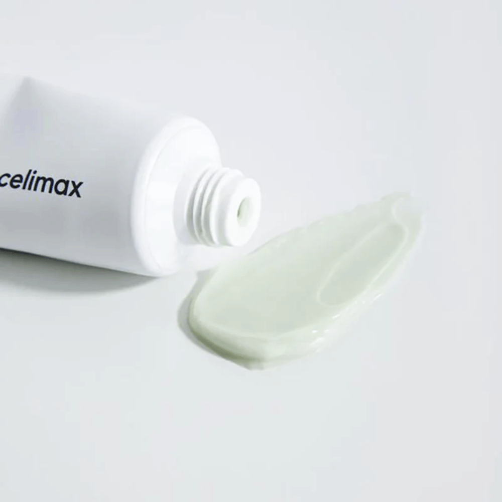 Celimax Noni Energy Repair Cream w białej tubce z niewielką ilością jasnozielonego kremu wyciśniętego obok tubki na białej powierzchni. Krem ma na celu odżywienie i naprawę skóry.