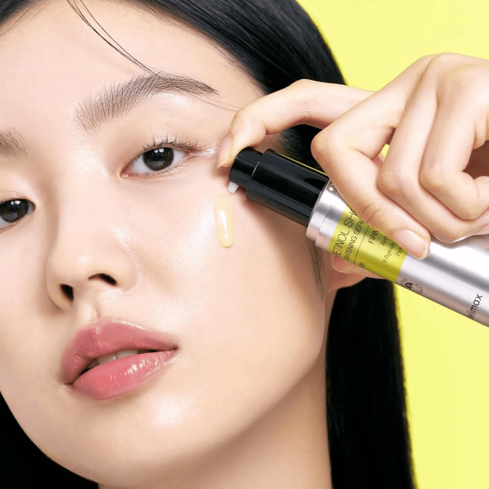 Modelka aplikuje The Vita-A Retinol Shot Tightening Serum od Tiam w okolicach oczu, koncentrując się na blasku skóry i żółtej konsystencji serum.