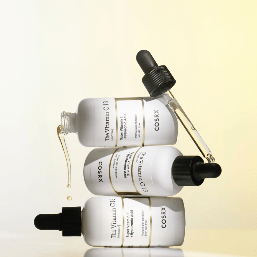 COSRX The Vitamin C 13 Serum z witaminą E i kwasem hialuronowym, trzy butelki z pipetą i kroplami serum z witaminą C przeciw nierównomiernemu kolorytowi skóry i dla blasku.