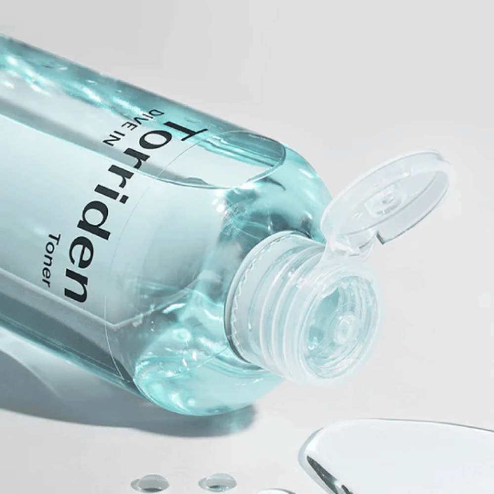Butelka DIVE-IN Low Molecule Hyaluronic Acid Toner 300ml obok szklanki wody, promuje Torriden i nawilżenie.