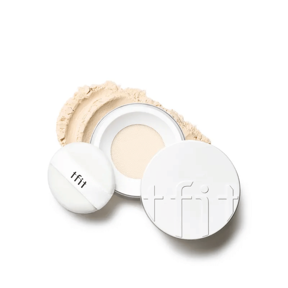 Otwarta puszka z TFIT Translucent Set Finishing Powder w odcieniu Skin Beige, z dołączonym puszkiem i puder do twarzy rozsypanym wokół.