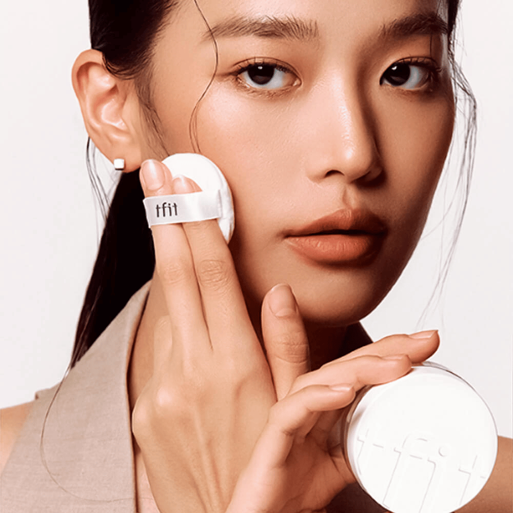 Kobieta nakłada TFIT Translucent Set Finishing Powder #02 Skin Beige za pomocą puszka, trzymając białą puszkę na puder z logo TFIT.