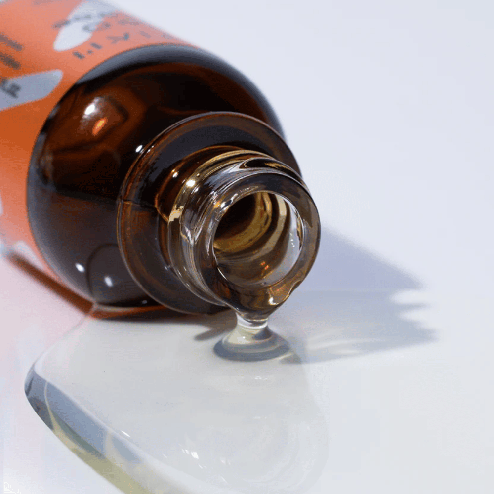 Zbliżenie na TIA'M Vita C Source-serum wypływające z brązowej szklanej butelki. Przejrzysta formuła serum podkreśla jego skoncentrowaną zawartość witaminy C dla promiennej skóry.