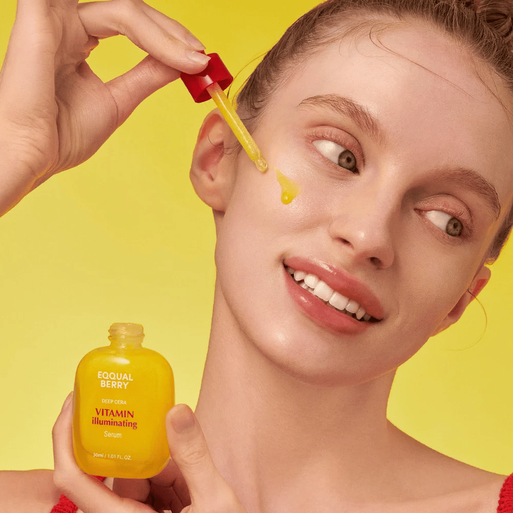 Uśmiechnięta kobieta aplikuje Equal Berry Vitamin Illuminating Serum za pomocą pipety. Świeża i promienna skóra na tle żywego żółtego koloru, który pasuje do koloru serum.