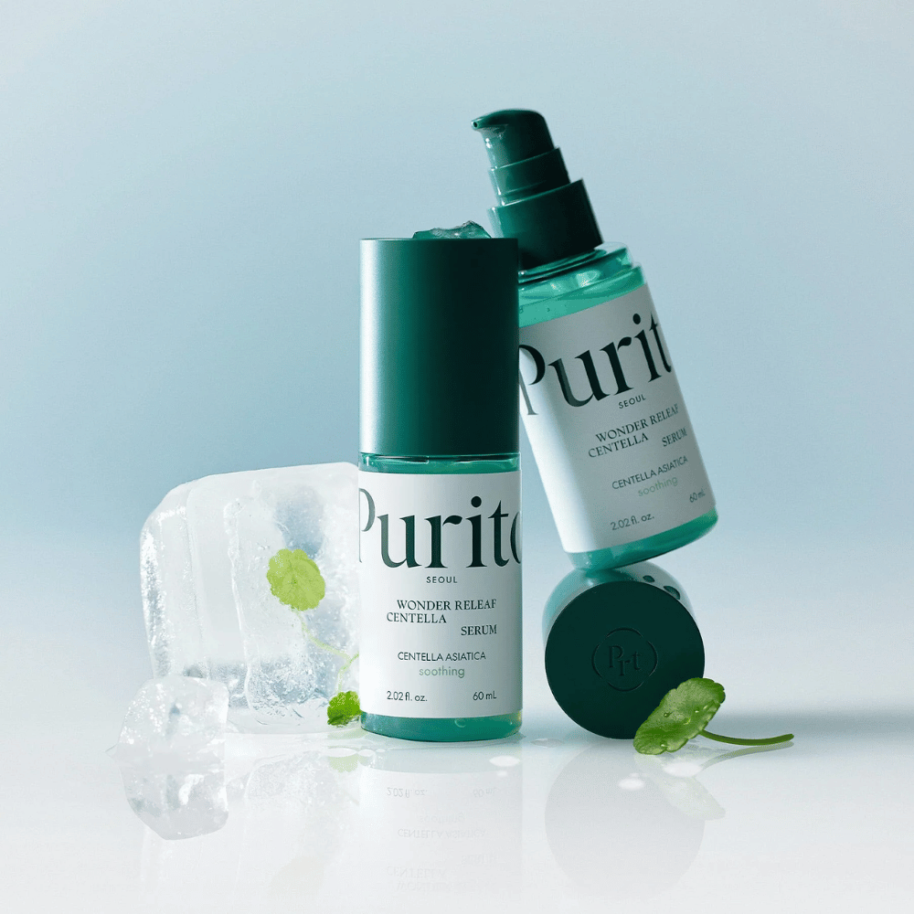 Dwie butelki Purito Wonder Releaf Centella Serum, jedna stojąca i jedna leżąca, otoczone kawałkami lodu z liśćmi centelli w środku oraz luźnym liściem na jasnoniebieskiej powierzchni.