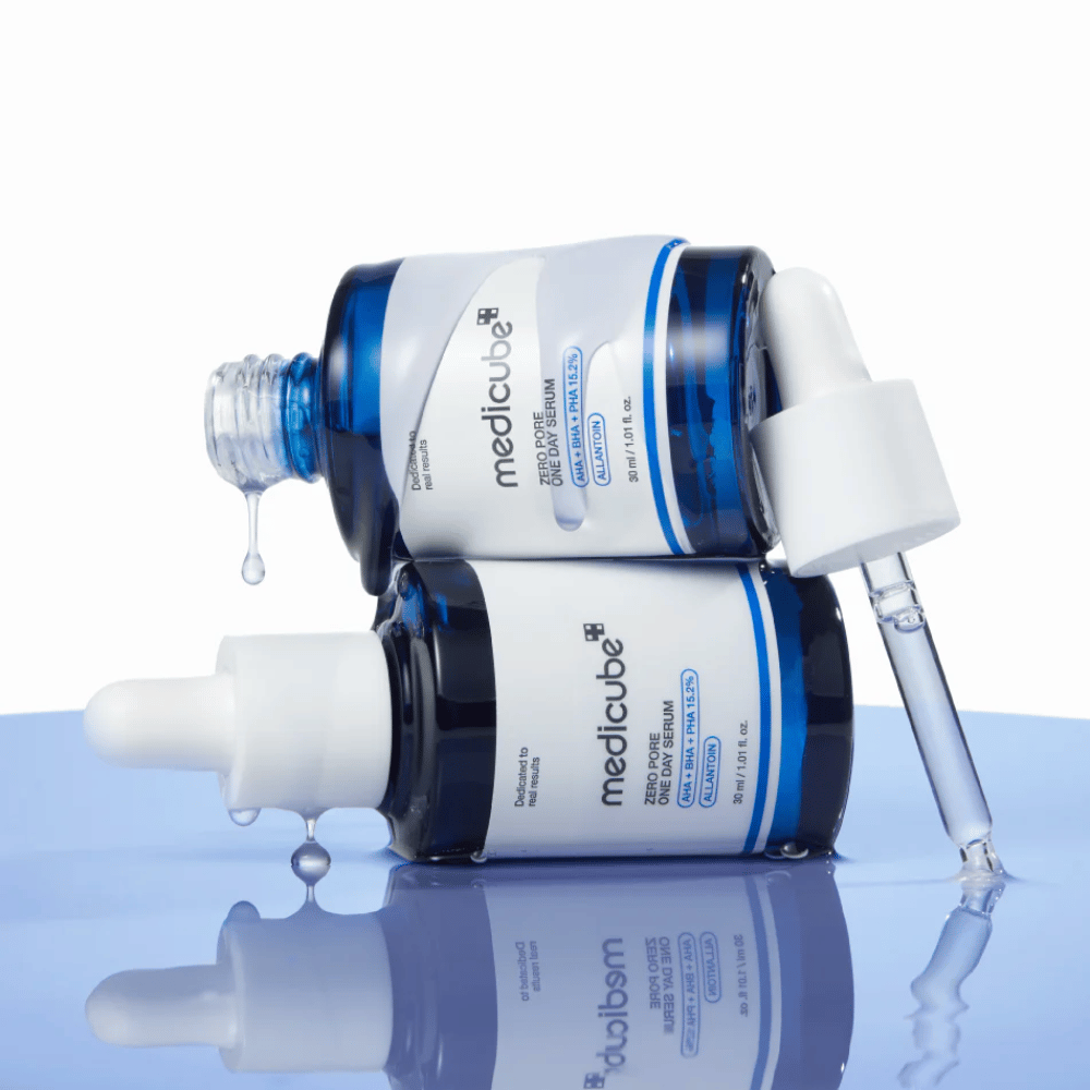 Dwie niebieskie butelki Medicube Zero Pore One Day Serum leżące obok siebie, z pipetami i kroplami serum na odbijającej niebieskiej powierzchni.