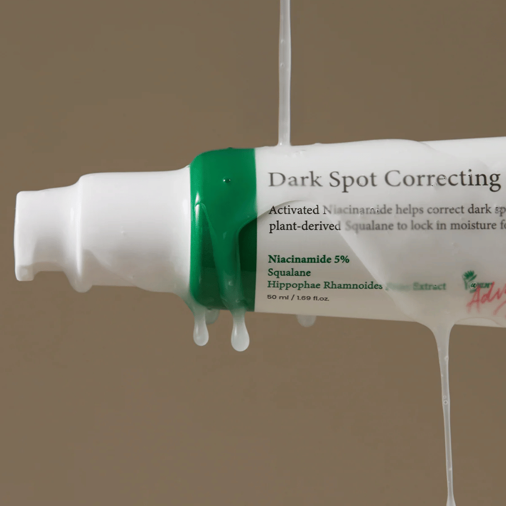 Zbliżenie na butelkę z pompką Axis-Y Dark Spot Correcting Glow Serum z białym opakowaniem i zieloną nakrętką, pokrytą płynącym przezroczystym płynem.