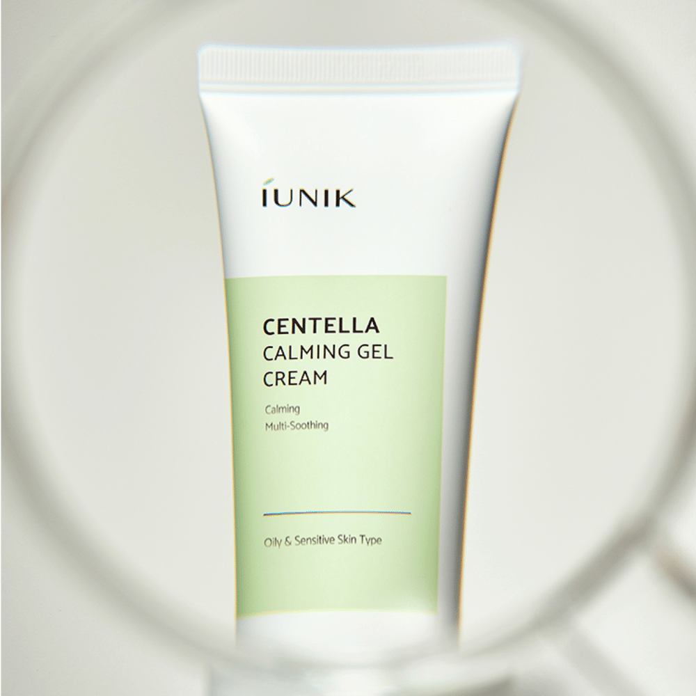 Tuba iUNIK Centella Calming Gel Cream z białym i jasnozielonym wzorem stoi pionowo, widziana przez okrągłą ramkę przypominającą szkło powiększające.
