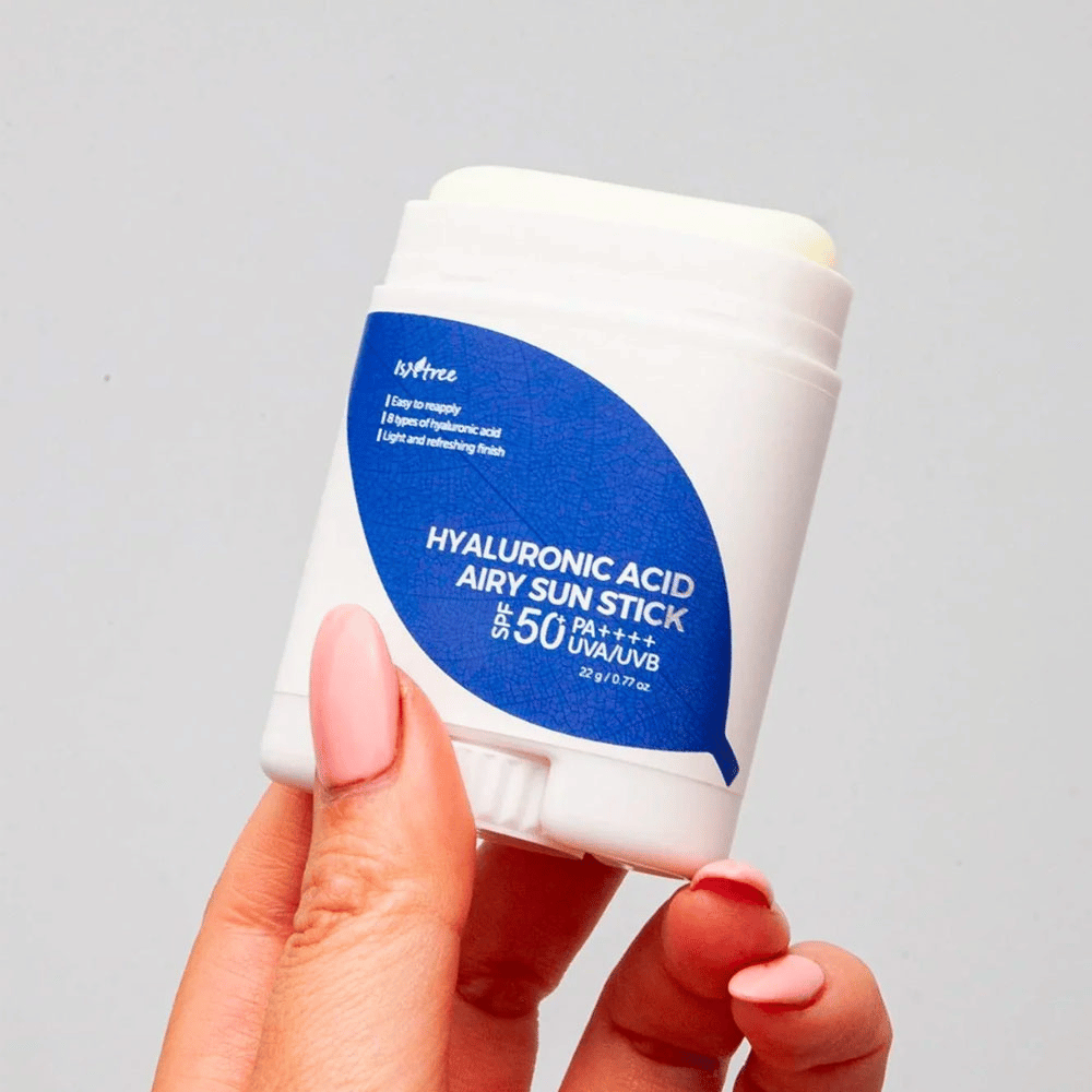 Ręka trzyma białą pałeczkę przeciwsłoneczną z niebieską etykietą od marki Isntree. Produkt nazywa się "Hyaluronic Acid Airy Sun Stick" i ma filtr przeciwsłoneczny SPF 50+ PA++++.