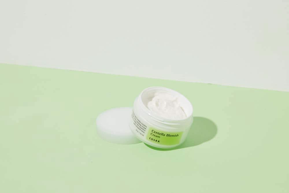 Słoik COSRX Centella Blemish Cream 30ml stojący na zielonej powierzchni.