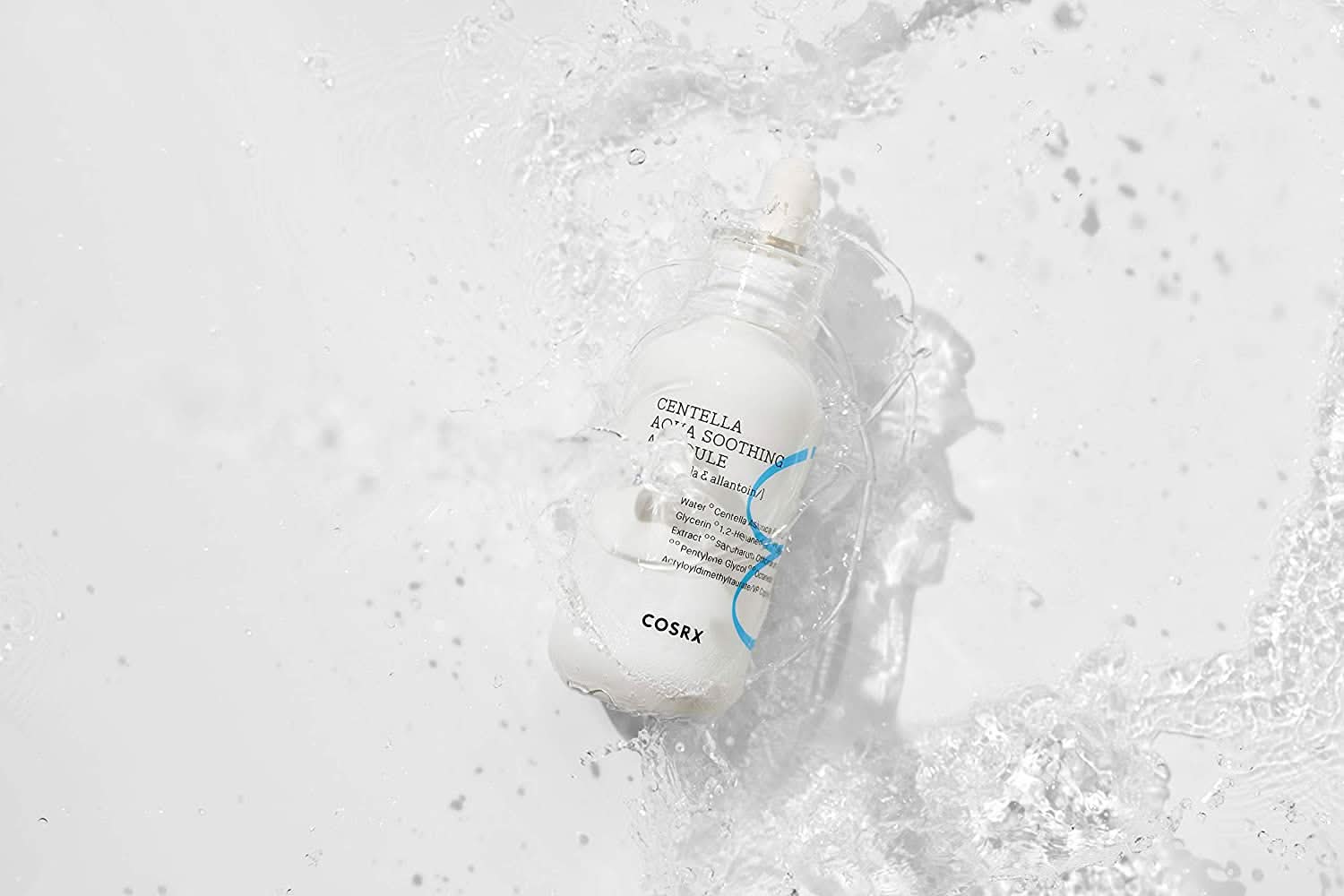 Butelka COSRX Centella Aqua Soothing Ampoule 40ml rozpryskująca się na białej powierzchni, zmniejsza zaczerwienienia i zapewnia łagodzące nawilżenie.
