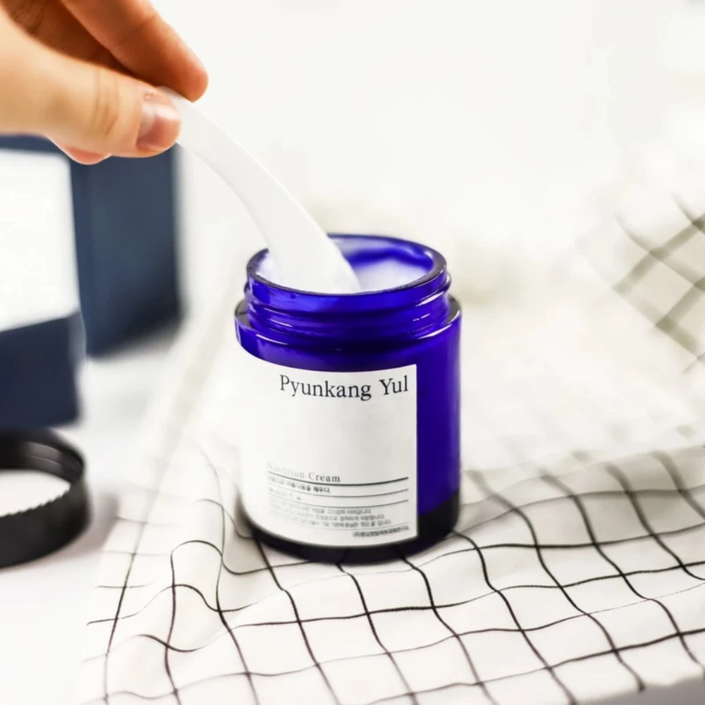 Osoba używa puszki Pyunkang Yul Nutrition Cream 100ml na stole.